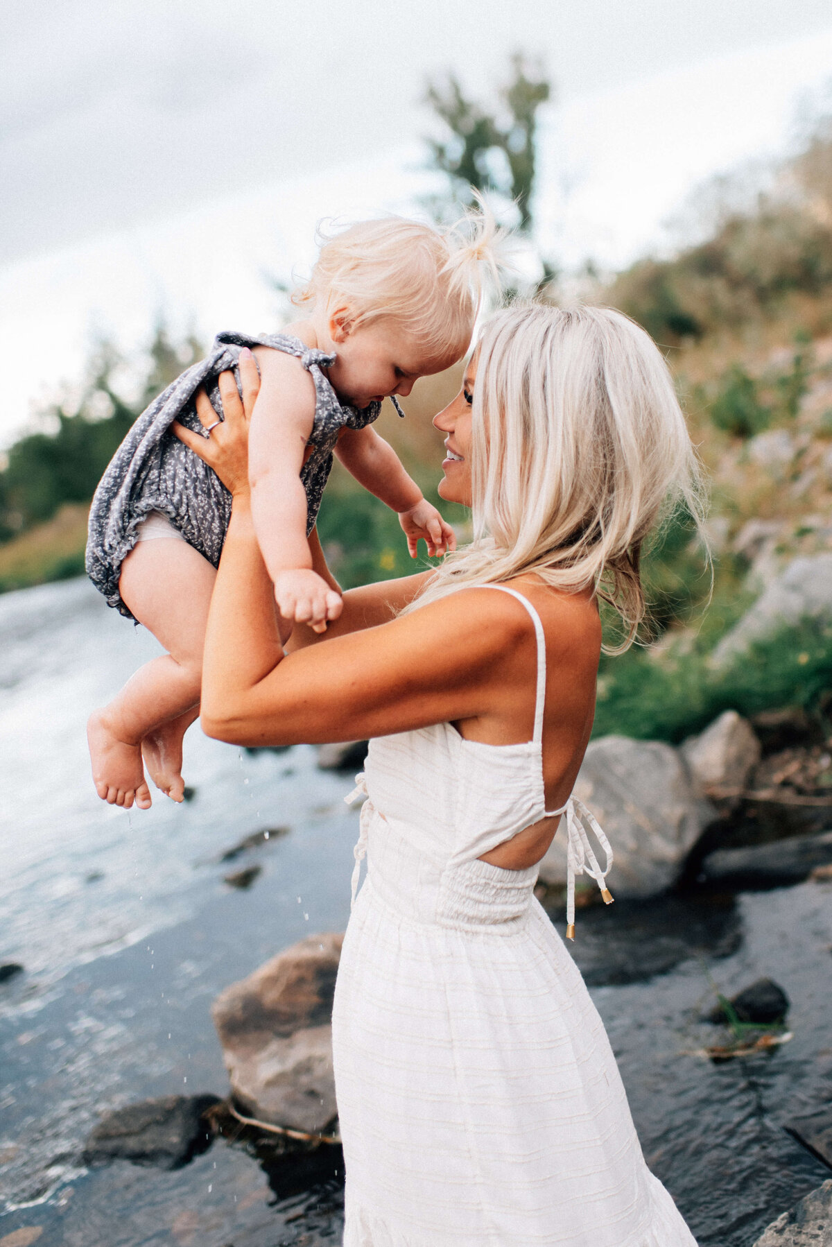 mom lifting her baby daughter up to her face next to a river in Denver