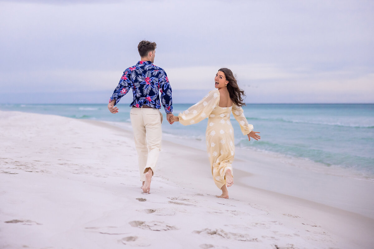 happy couple running down the beach holding hands after they just got engaged on Grayton Beach, Florida.