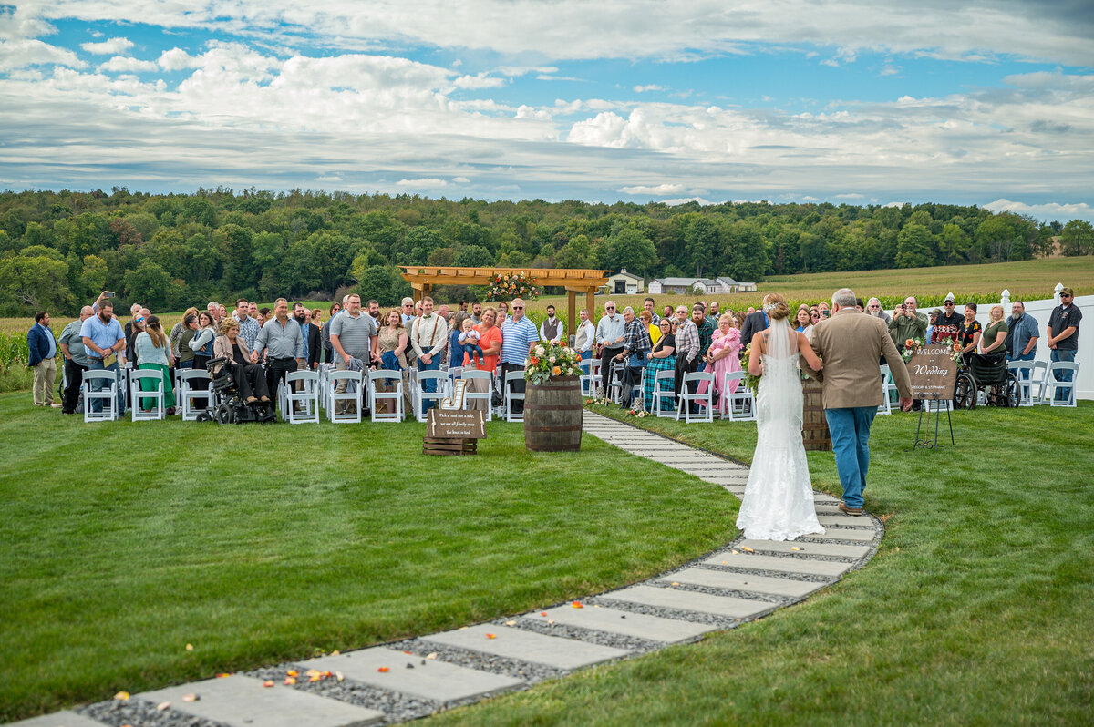 Dad walking bride down isle during an outdoor wedding ceremony.