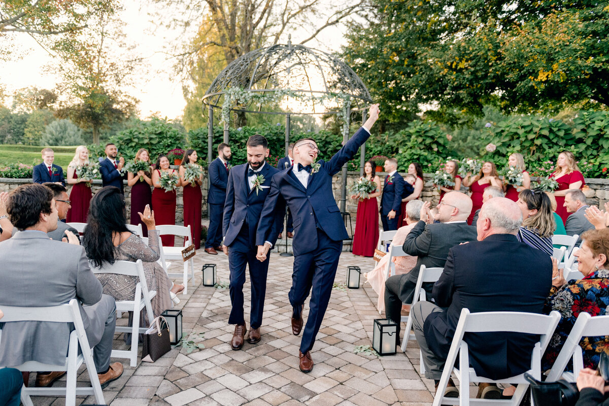 grooms walk hand in hand down aisle at outdoor Hudson Valley wedding ceremony
