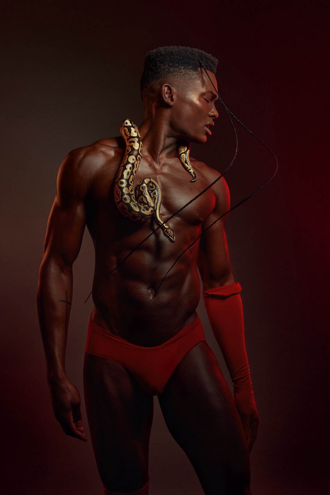 Studio portrait of Julian Woodhouse in an elaborate red outfit, showcasing a dramatic pose, photographed by Ylva Erevall.