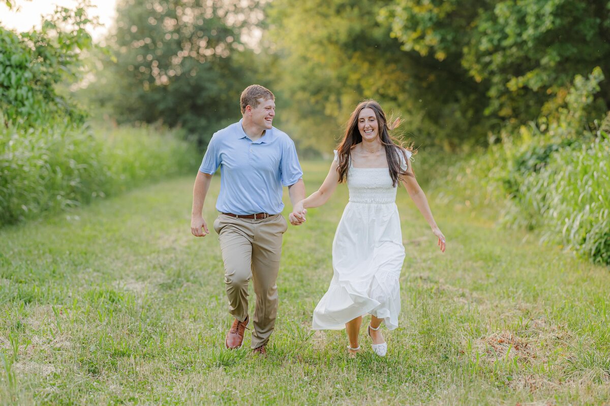 A happy newly engaged couple holds hands and skips through a forest trail