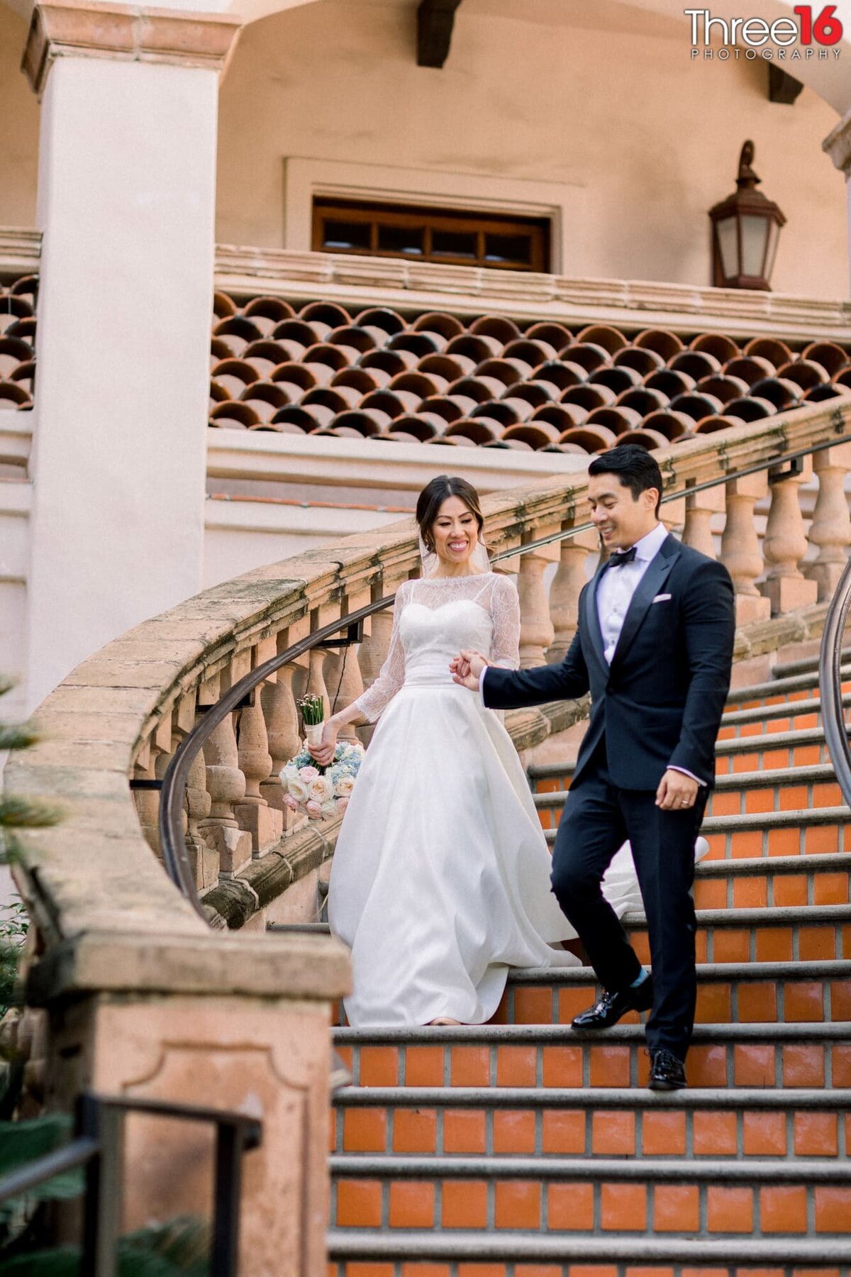 Groom leads his Bride by her hand as they walk down the spiral staircase