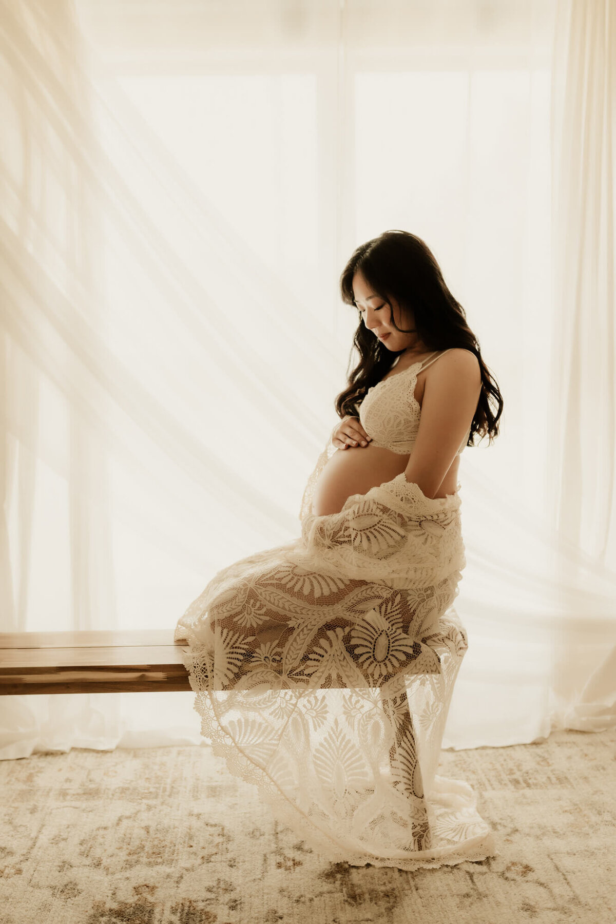 Expecting mother kneeling on a bench and wearing a lace bralette and kimono.