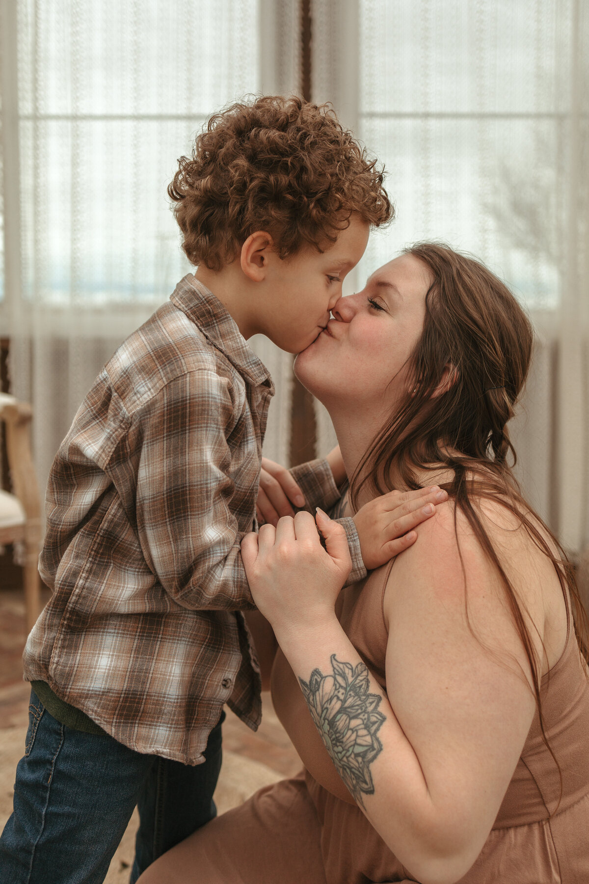 little boy with curly hair and plaid shirt kissing mom wearing tan dress in firestone colorado