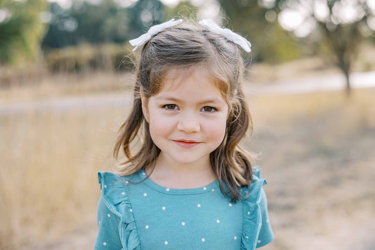 little girl in blue dress with bows in her hair smiling at the camera