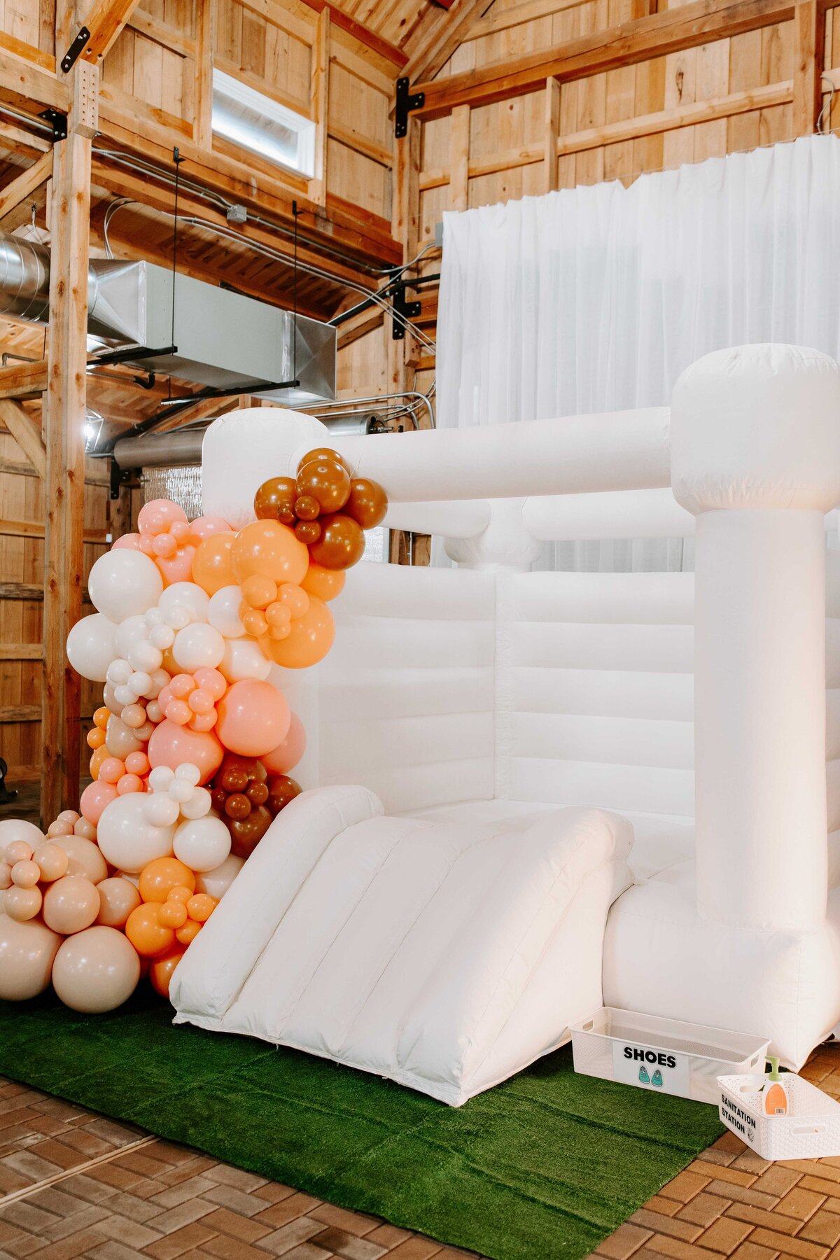 Bounce castle with orange, pink, white balloon arch