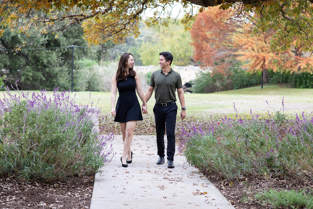 An Austin wedding photographer captures a couple strolling down a path in a park, capturing their candid moments against the backdrop of nature.