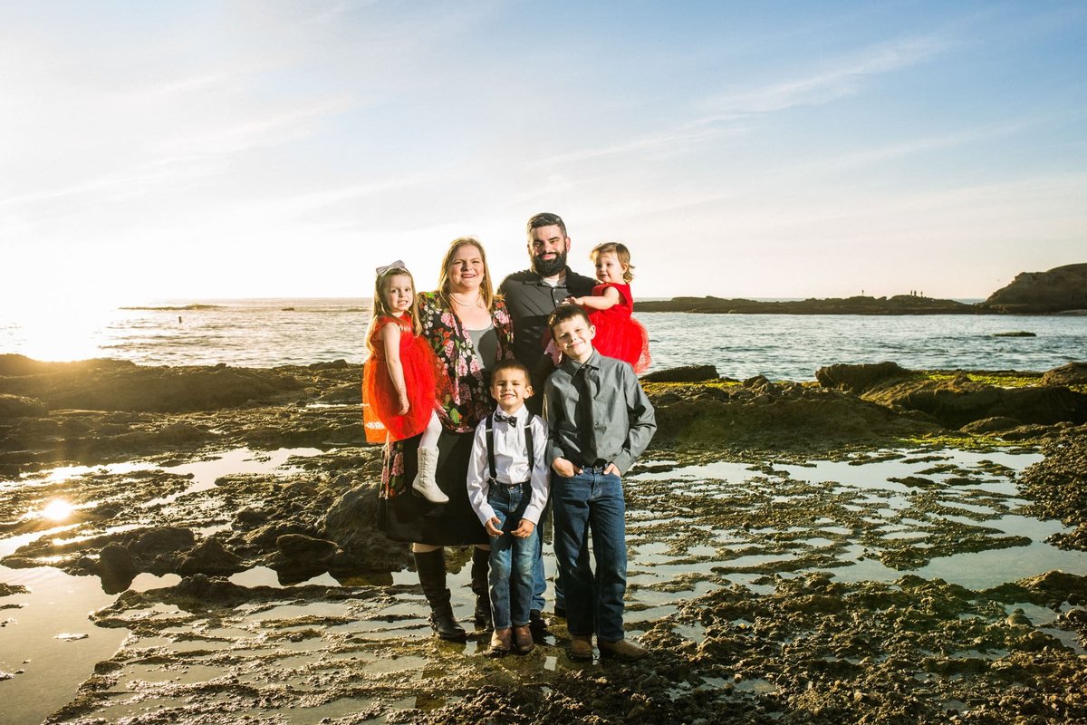 Parents pose for photos with their four children along the rocks at the beach