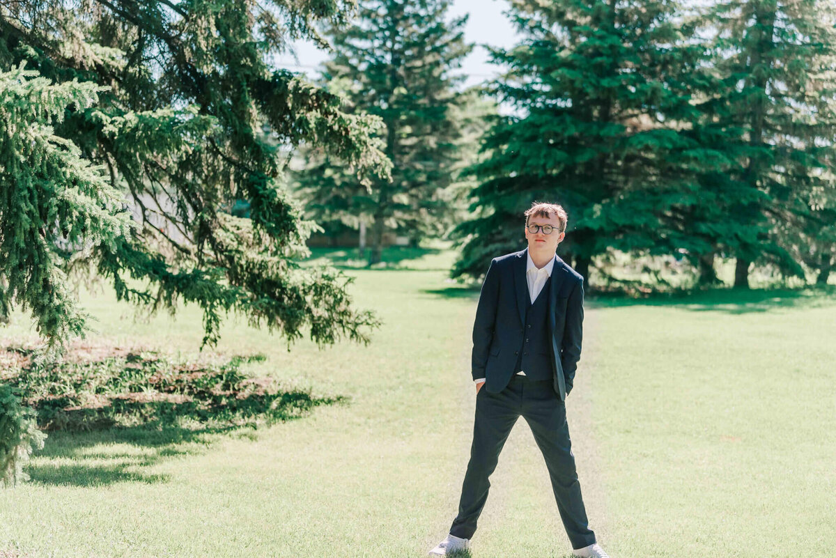 A young man standing on some grass surrounded by trees.