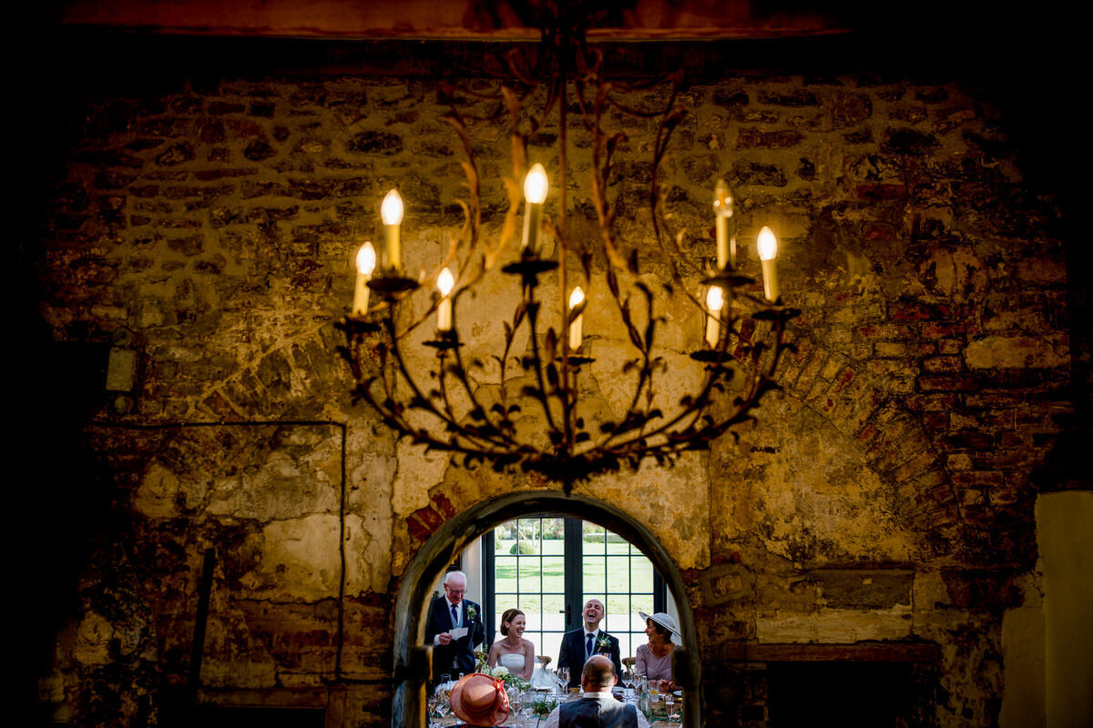 speeches photographed through a doorway at middleton lodge. father of bride doing speeches and mother, bride and groom all laughing. during wholesome moment.
