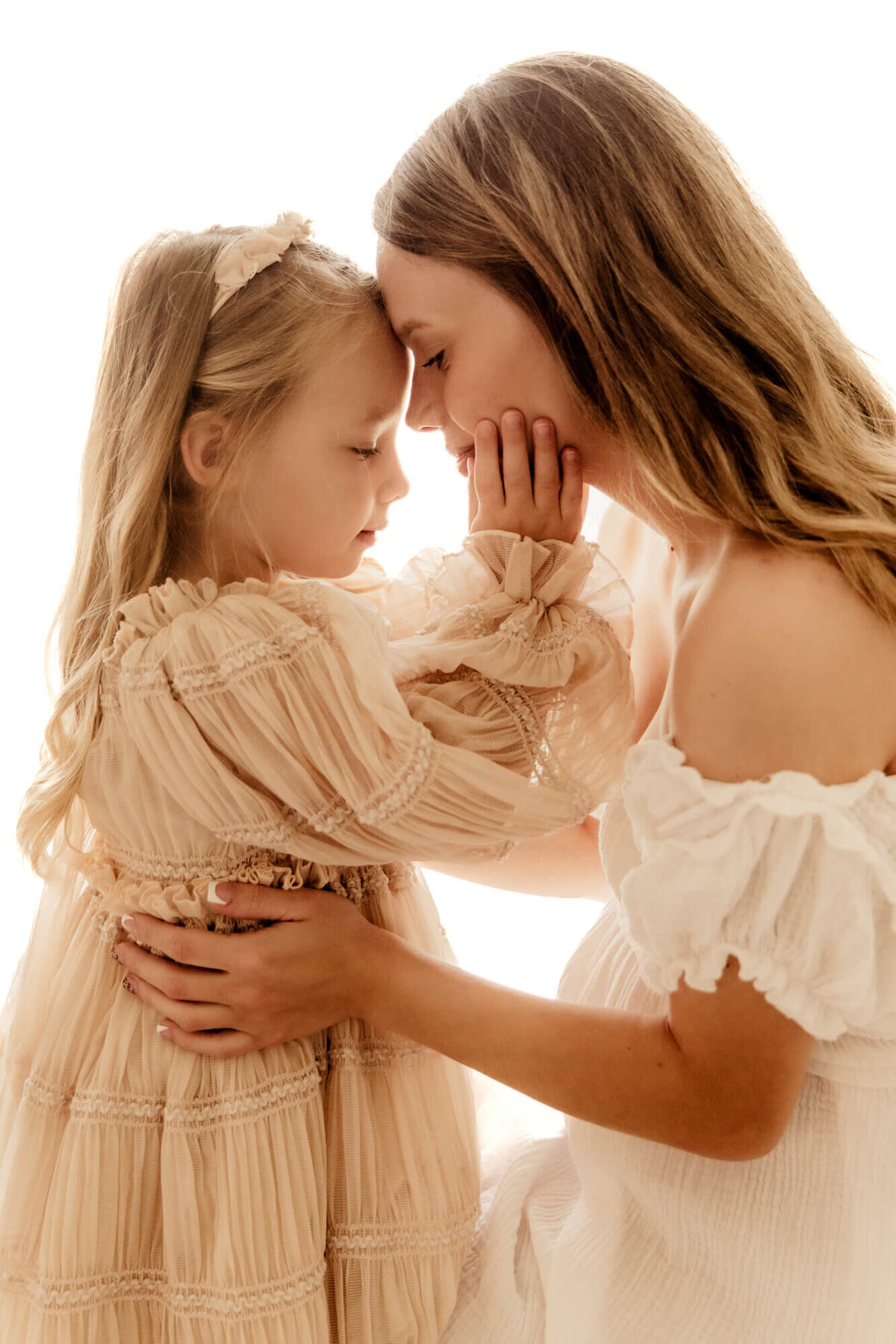 Daughter cups her mother's face in her hands while they both close their eyes.