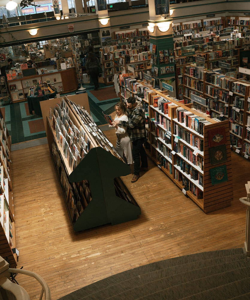A book-loving couple shares a romantic moment among the bookshelves during a library engagement session in Spokane, Washington.