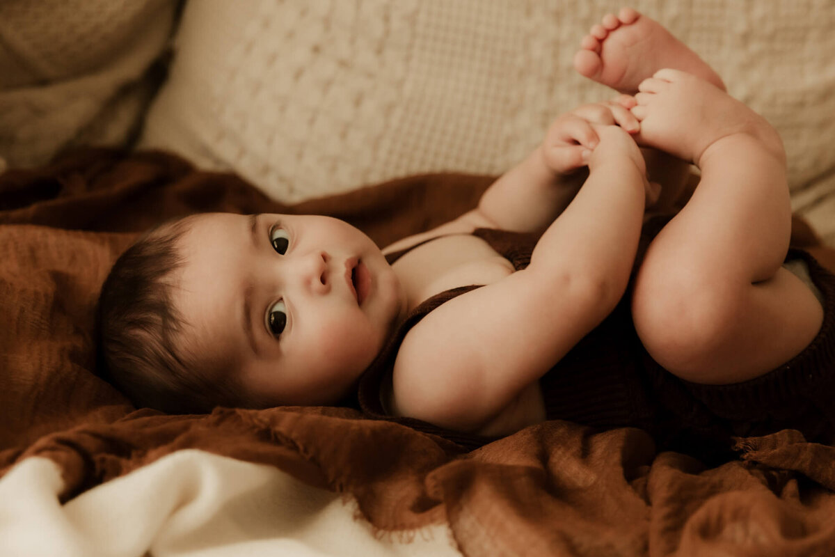 Little boy laying on his back while wearing a brown romper.