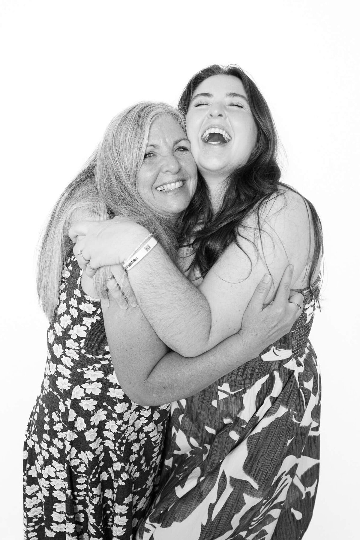 Two women sharing a joyful hug and laughter, photographed in a modern black and white portrait by Monochrome Portraits, a Phoenix photo booth experience.