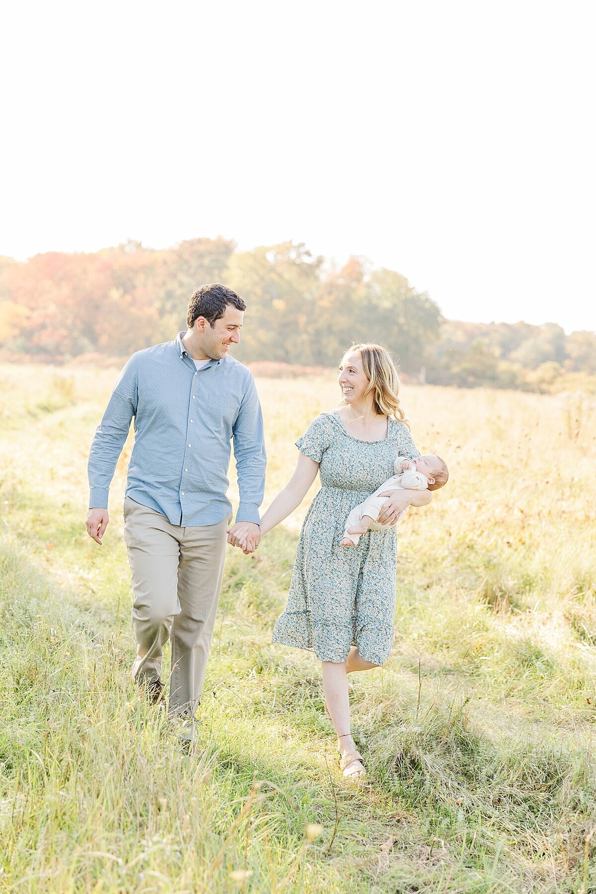 parents walk through field with baby during outdoor newborn photo session in Natick Massachusetts with Sara Sniderman Photography