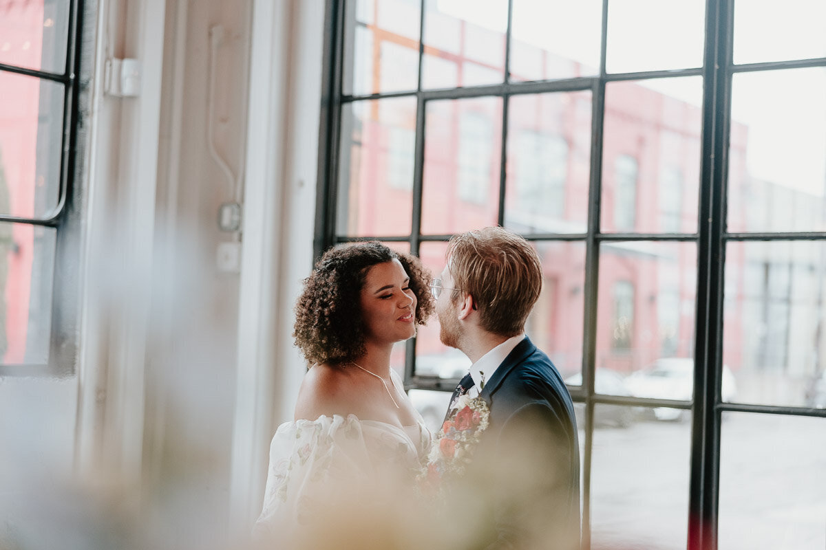 Newlyweds stand in a window and lean in for a kiss