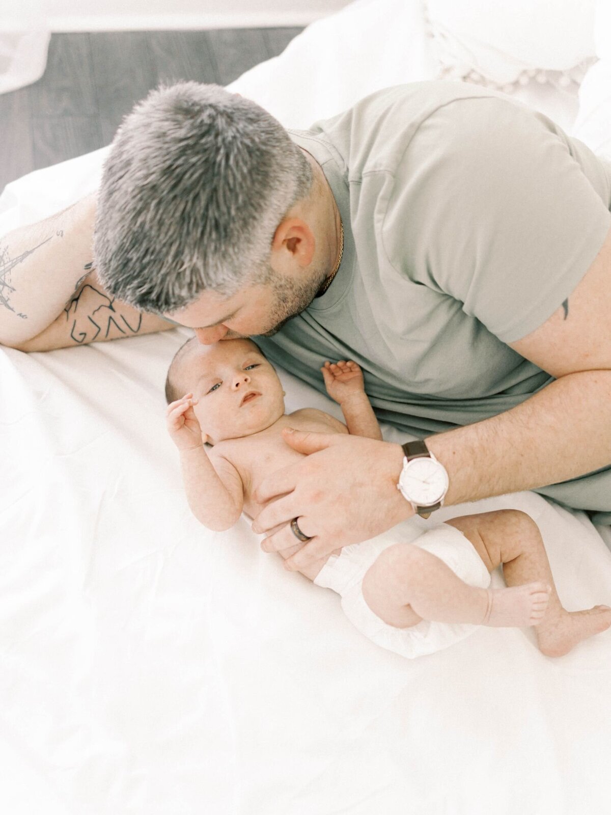 Man lays on bed with newborn baby for Richmond Newborn Photography session