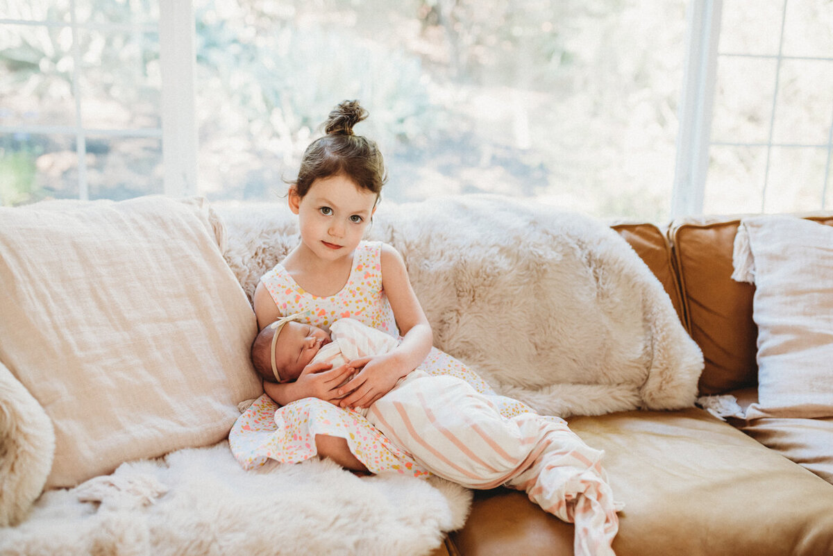 Big sister holds newborn baby sister on couch