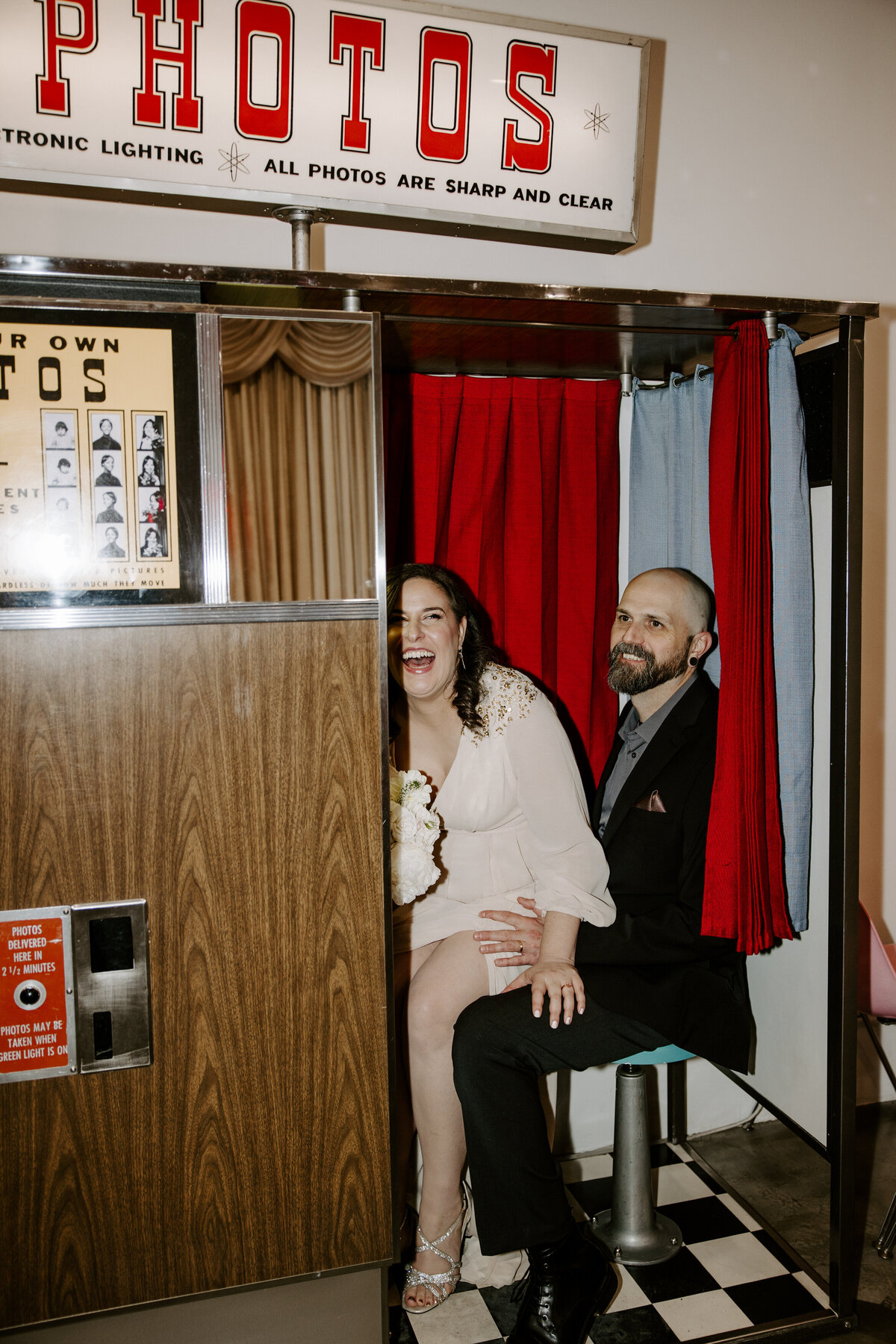 A couple poses in a photo booth, laughing.