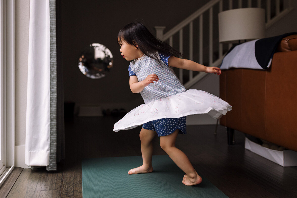 girl in white dress twirling by window in her family room