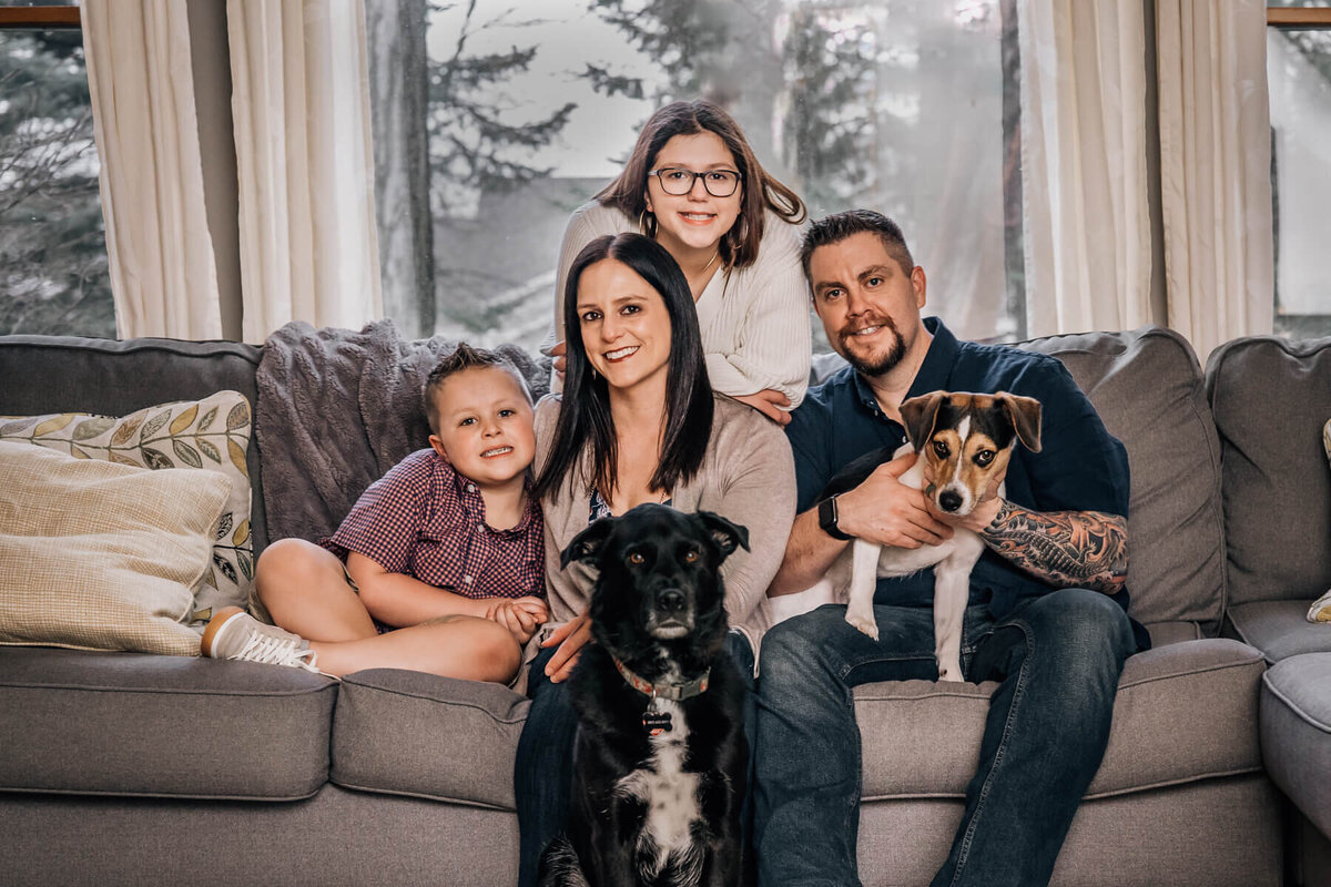 A family sits on their couch with their two dogs during an in home photo session.