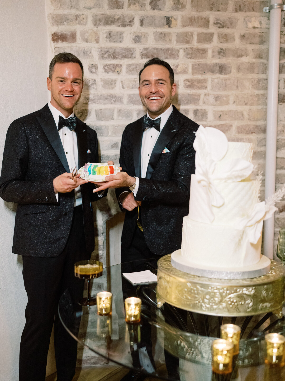 Two men dressed in formal attire proudly present a beautifully designed pride wedding cake, symbolizing love and unity during their celebratory event marked by happiness and connection.