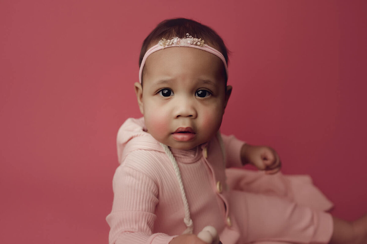 a one year old girl closeup shot on a pink backdrop