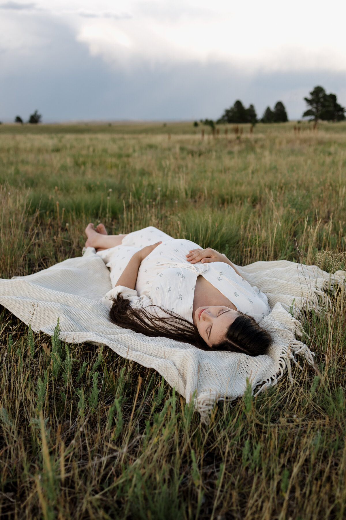 Expectant mother laying on blanket while looking towards the mountains with hands on belly