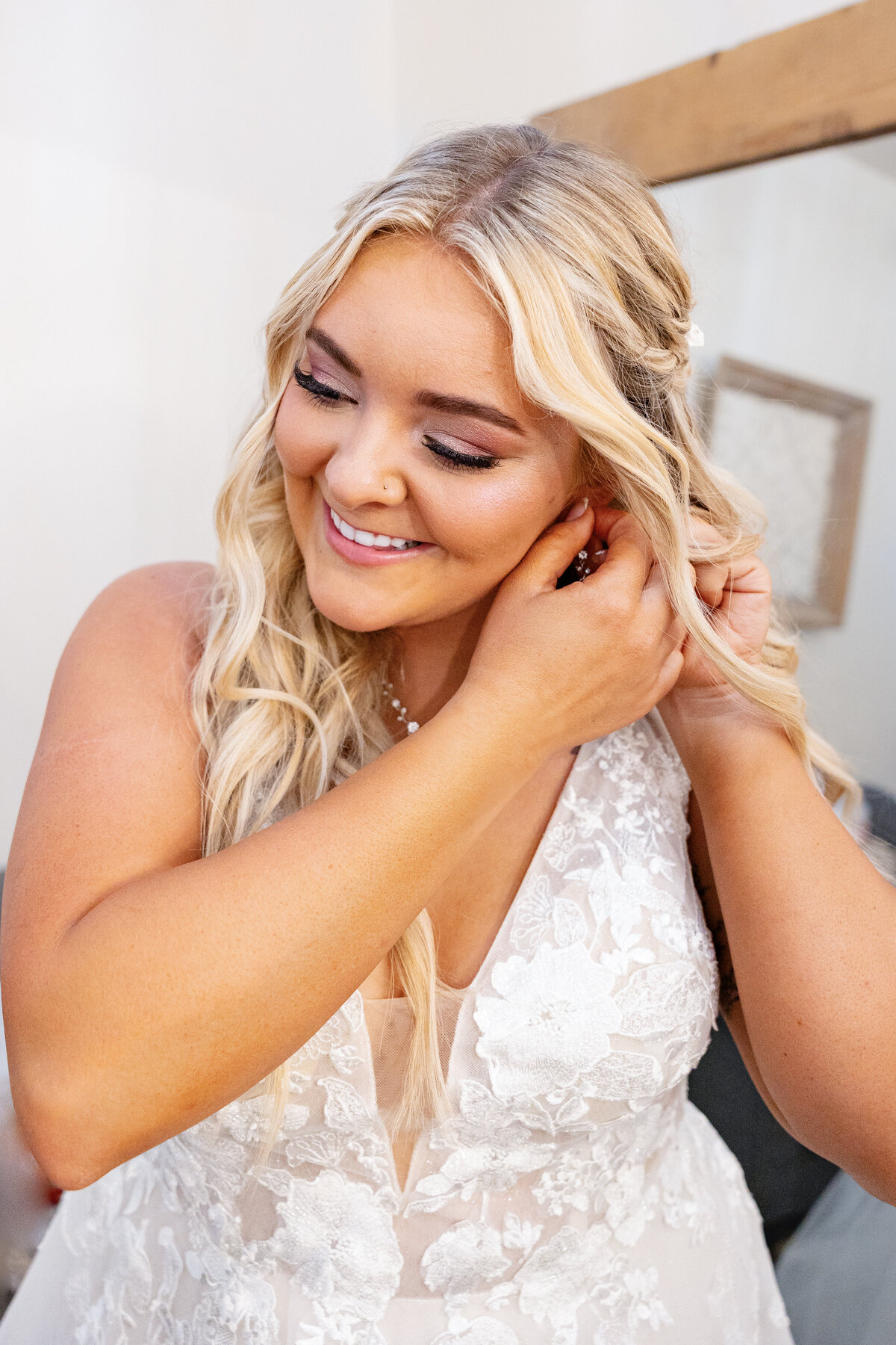 The bride, glowing with happiness, adjusts her earrings as she prepares for her big day. Her soft curls and intricate lace gown complete her ethereal look.