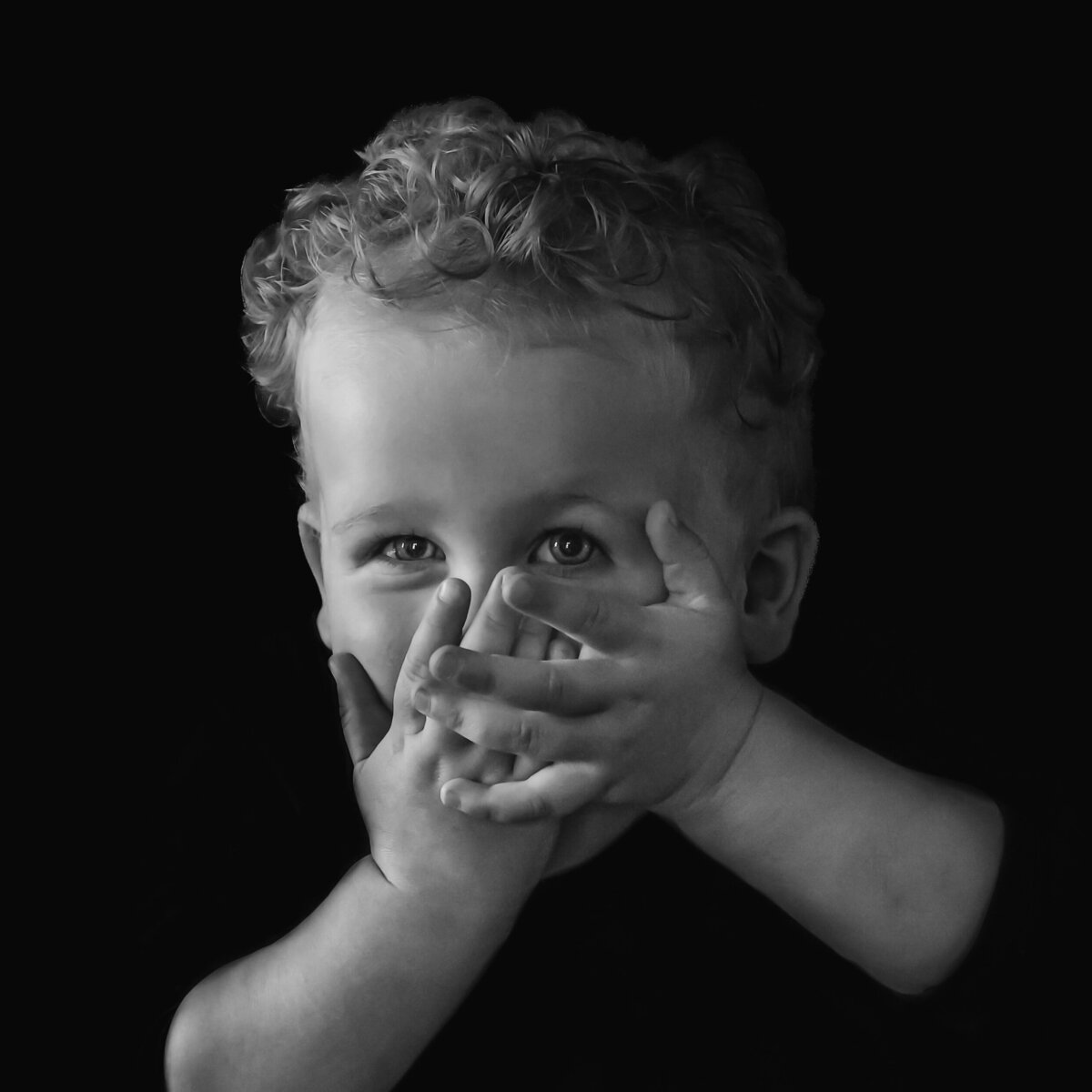 Een zwart-wit portretfoto van een lachend jongetje, gefotografeerd tegen een donkere achtergrond.