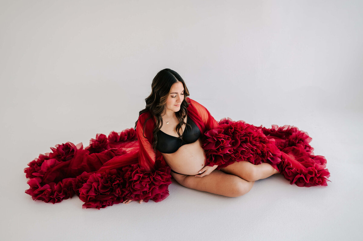maternity picture of pregnant mom sitting in red robe in studio