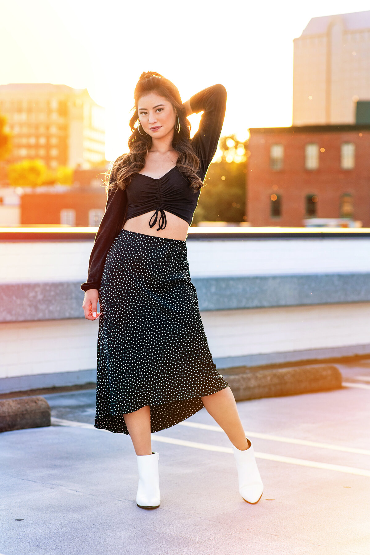 Senior girl at sunset on a rooftop wearing black midi skirt and white ankle boots.