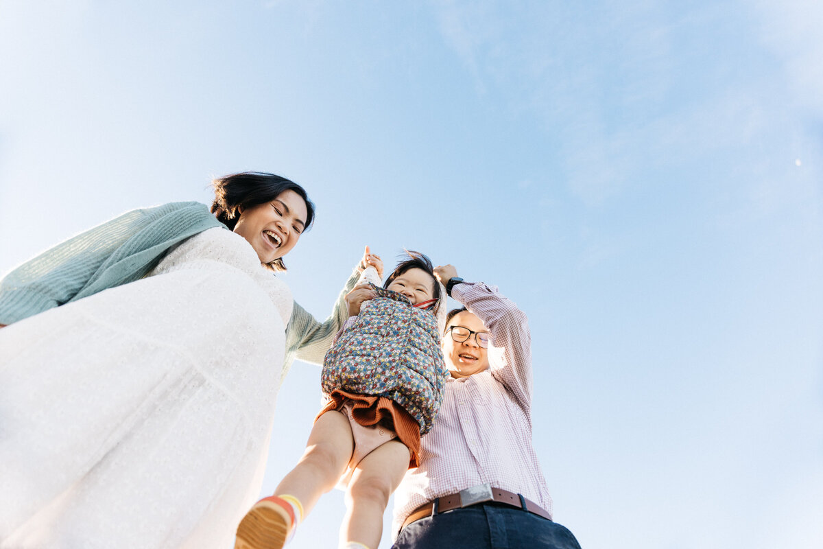 Mother and father are tossing their toddler girl in the air.