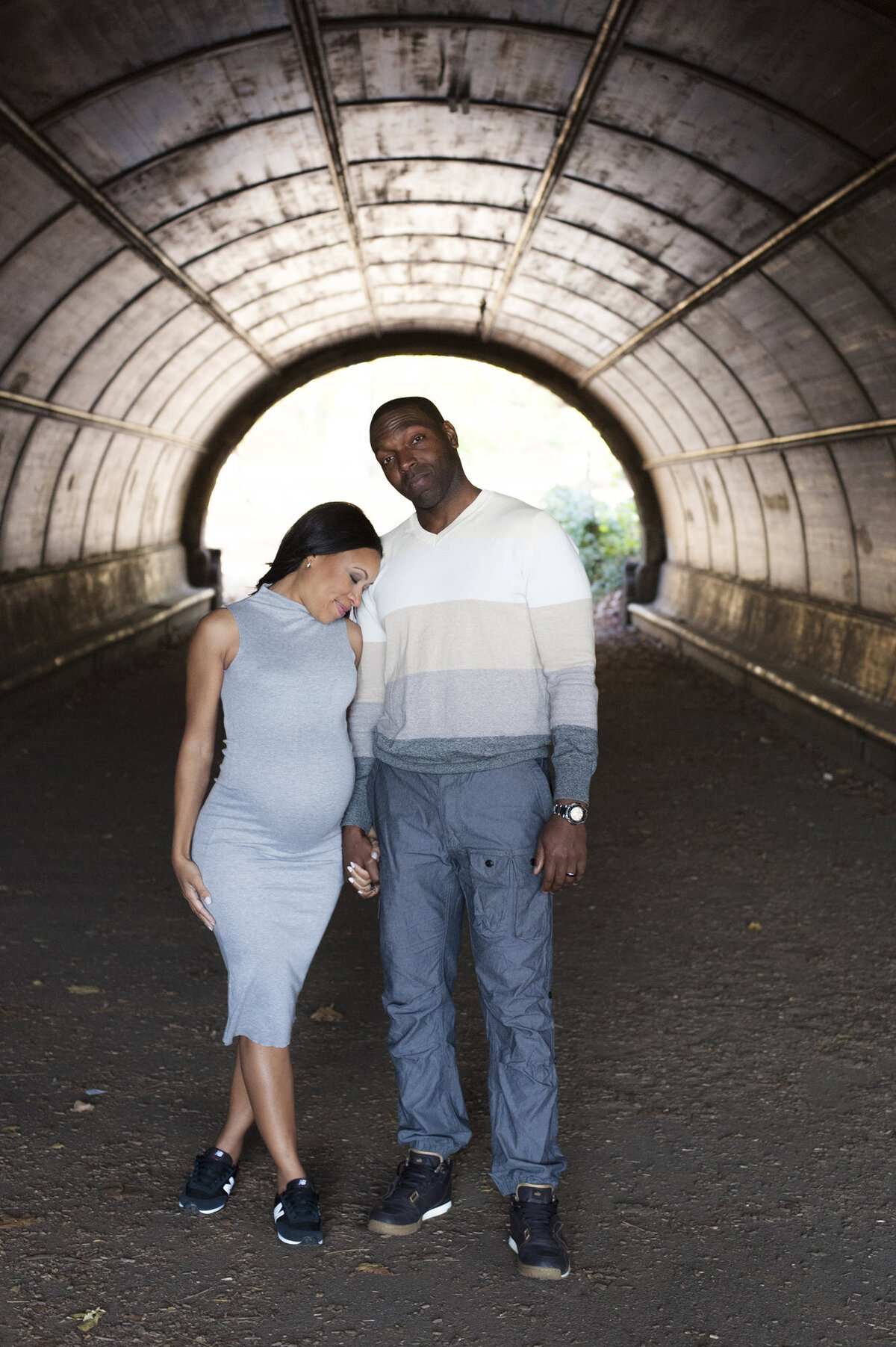 A pregnant couple holding hands and standing in a tunnel 
