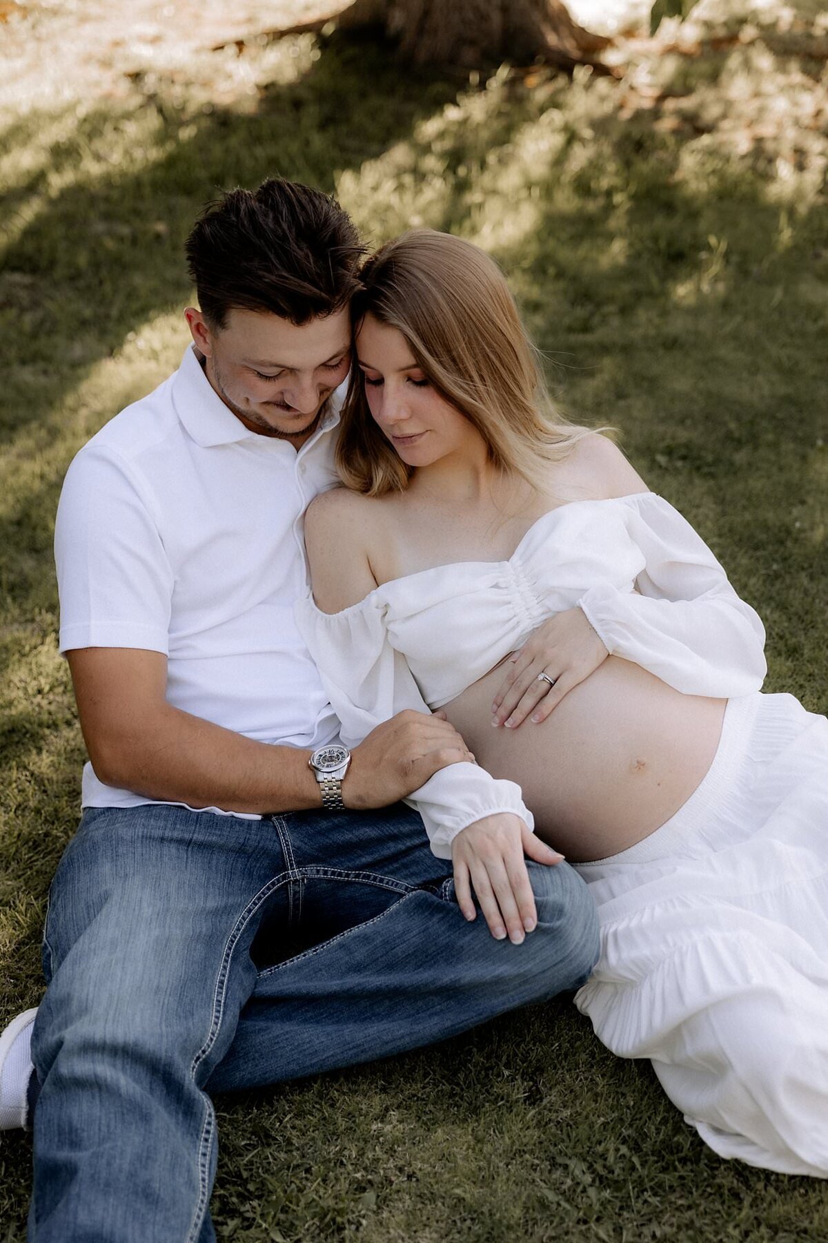 pregnant couple sitting on grass, mom belly is exposed to showcase pregnancy
