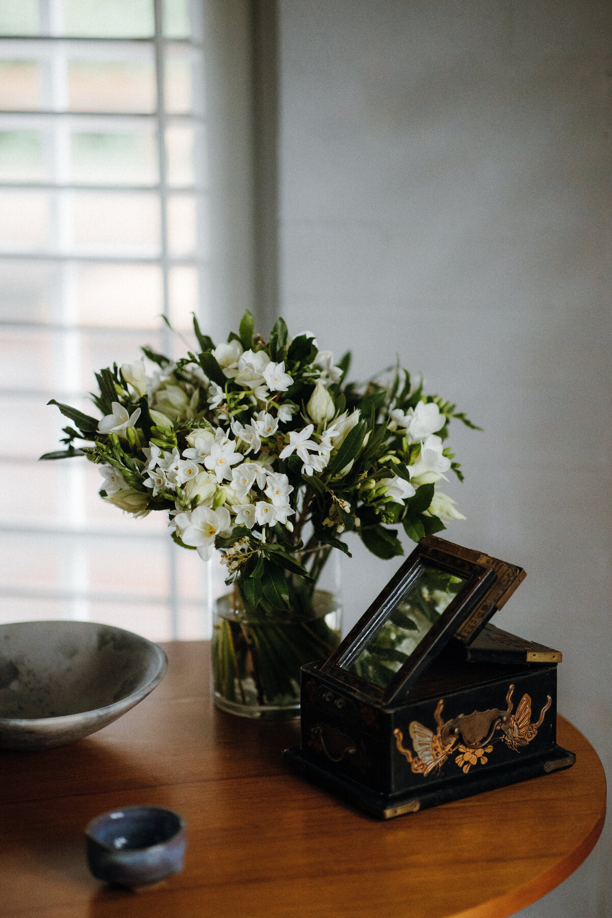 A vintage box, a bowl, and a bouquet of flowers in a glass vase.