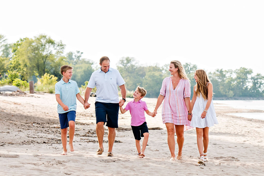 Family walks across the beach hand in hand smiling at one another.