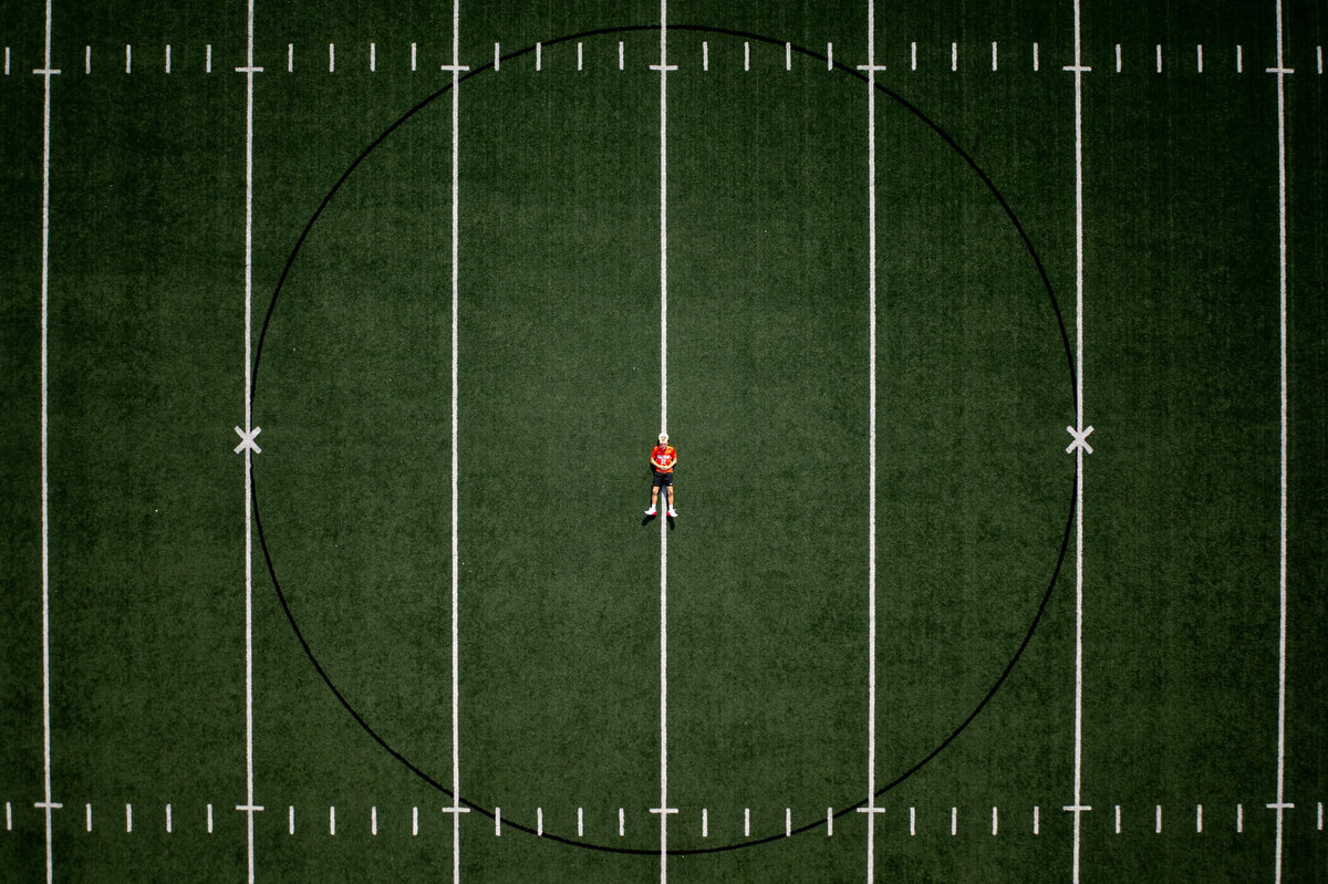 drone senior portrait of a senior laying on a soccer field, dead center, laying down and resting his head on a soccer ball