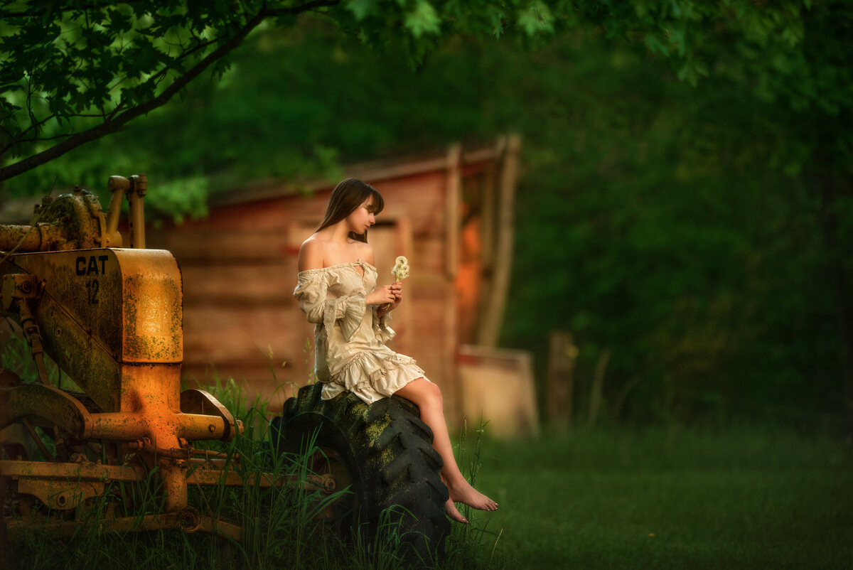 Barefoot girl in a farm sitting on a tractor tire and holding  dandelions.