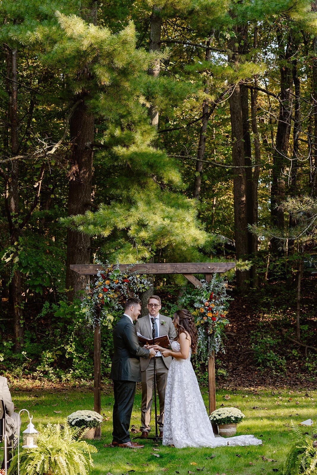 A bride and groom stand in front of a flower covered arbor during their wedding ceremony.