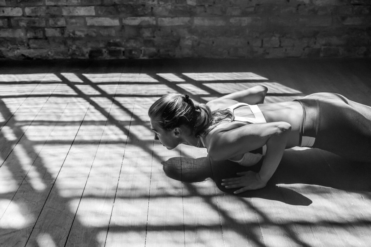 Woman performing a push-up on a wooden floor with dramatic window shadows, showcasing strength and core engagement during a workout.