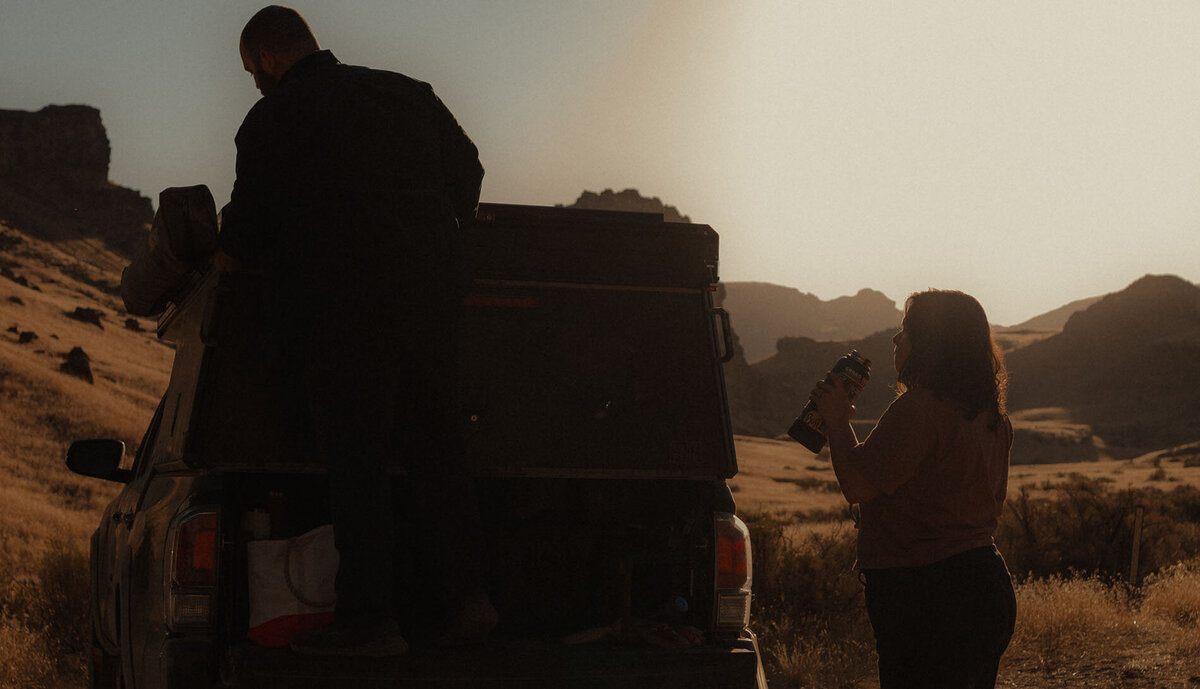 a woman stands next to her truck and drinks water under the sunset in Moab, Utah