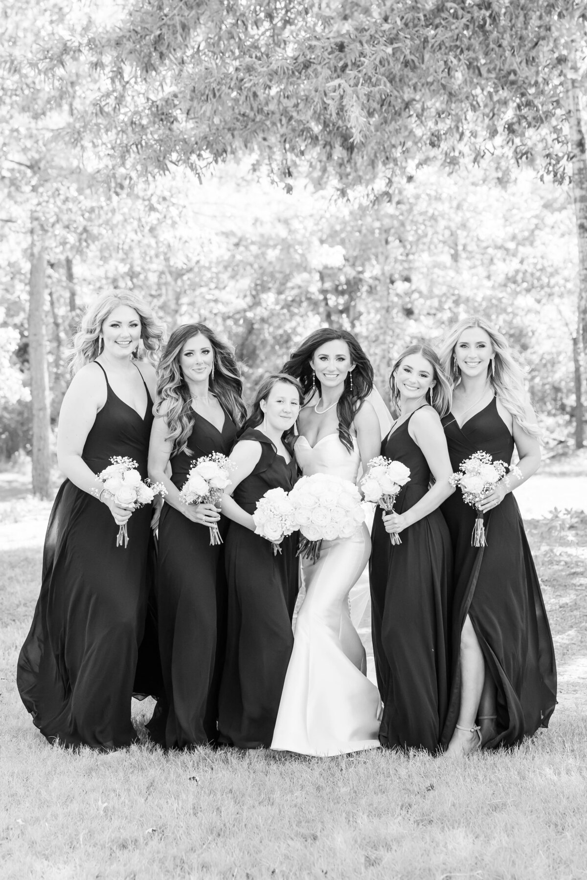 Black and white image of a bride and her bridesmaids standing among the trees.