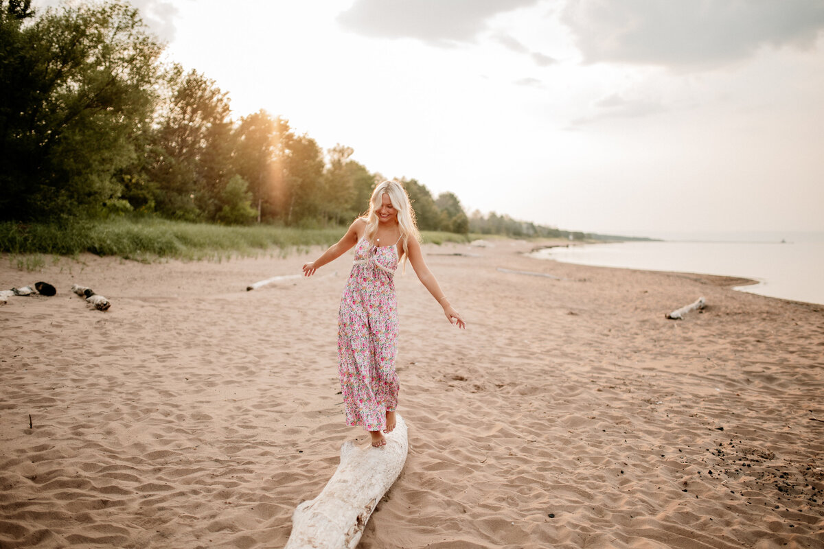 Milly playfully balances on a piece of driftwood on the beach during her Duluth senior portraits.