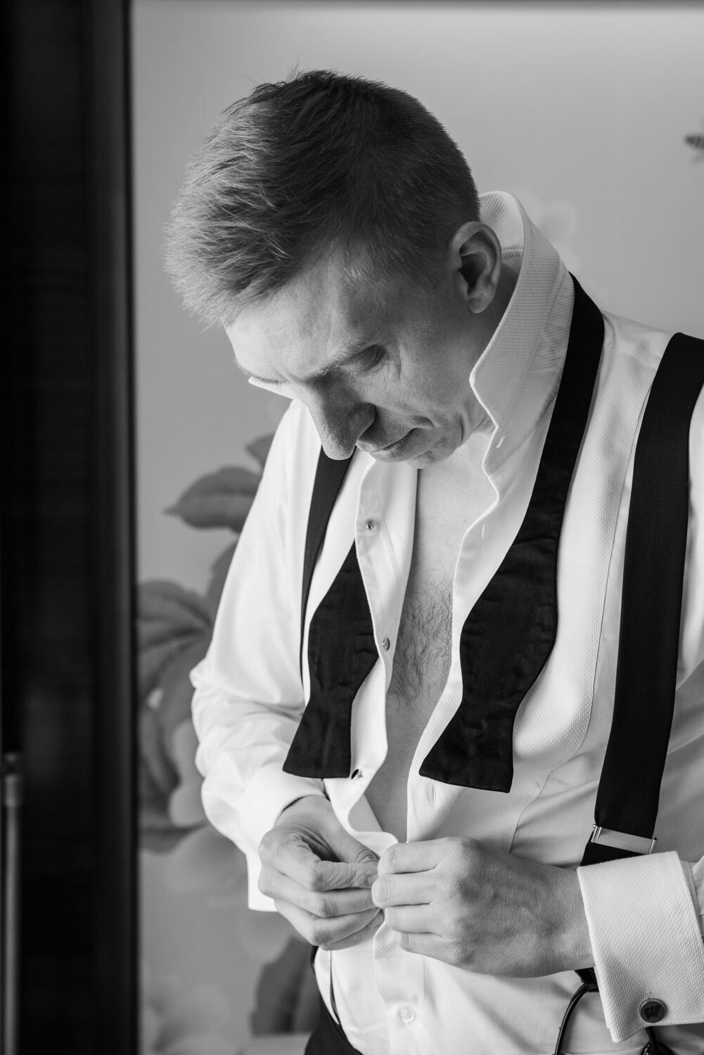 A man wearing a bow tie and suspenders looks down