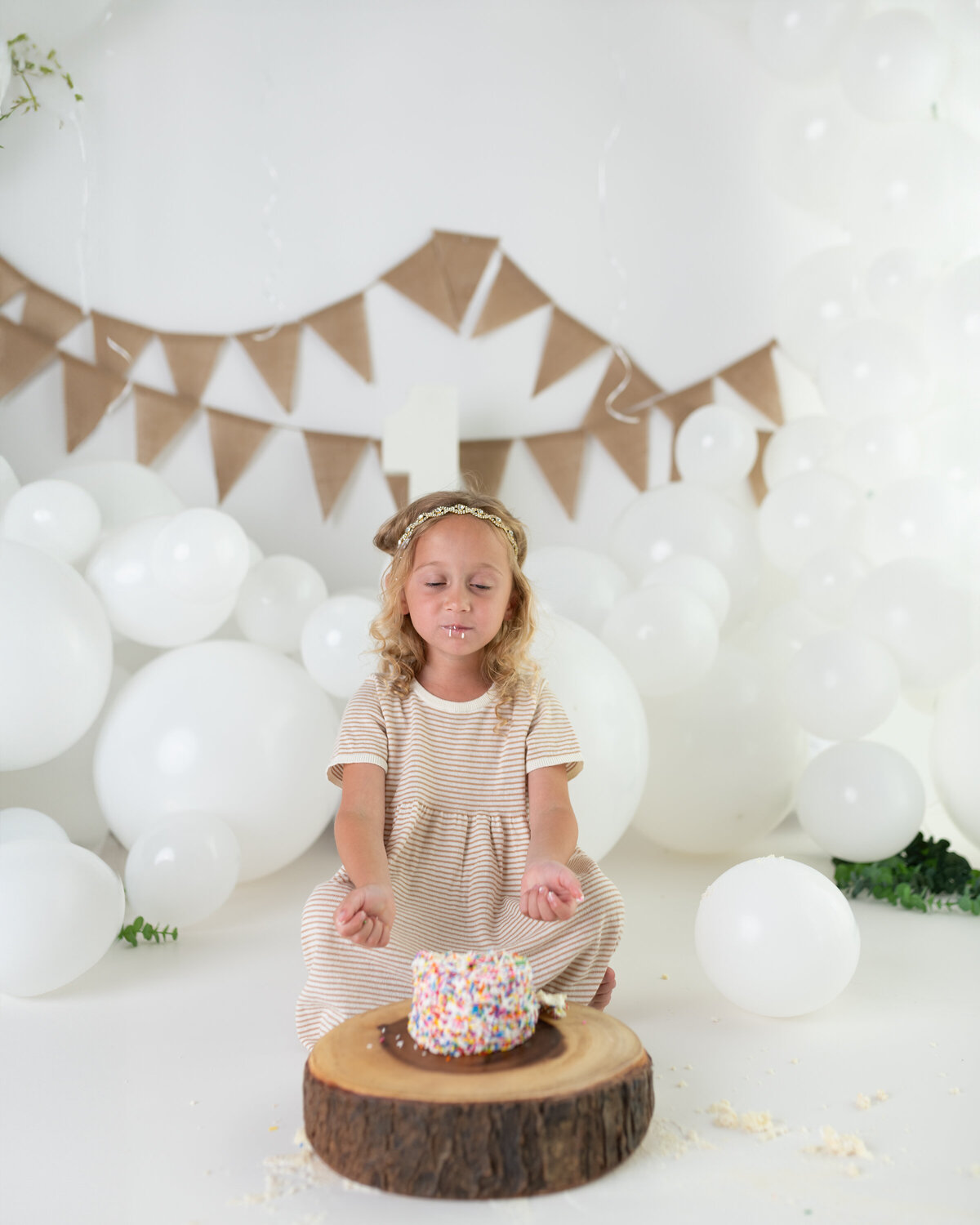Cake smash milestone portrait of a five-year-old with a sprinkle-covered cake and a serene pose before the fun begins.