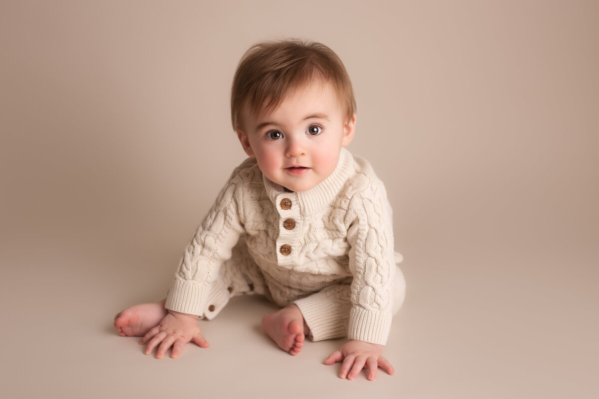 Baby sitting posing for photo in cream knitted romper