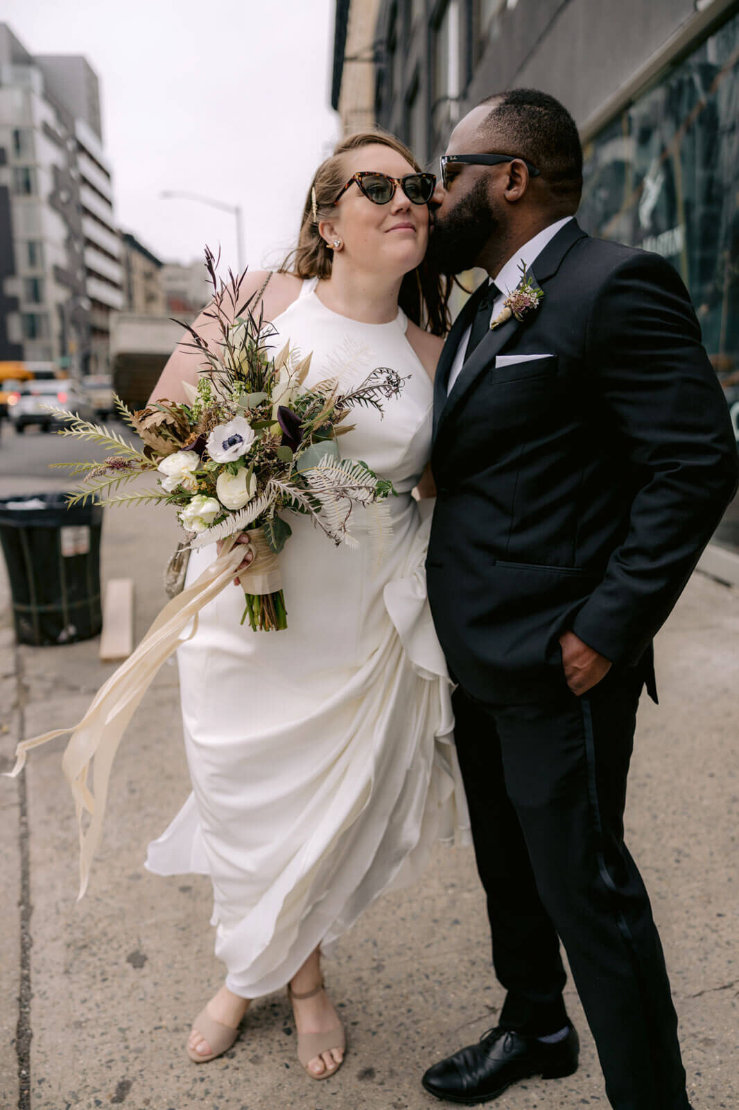 The groom is kissing the bride in the cheeks in the streets of New York City.