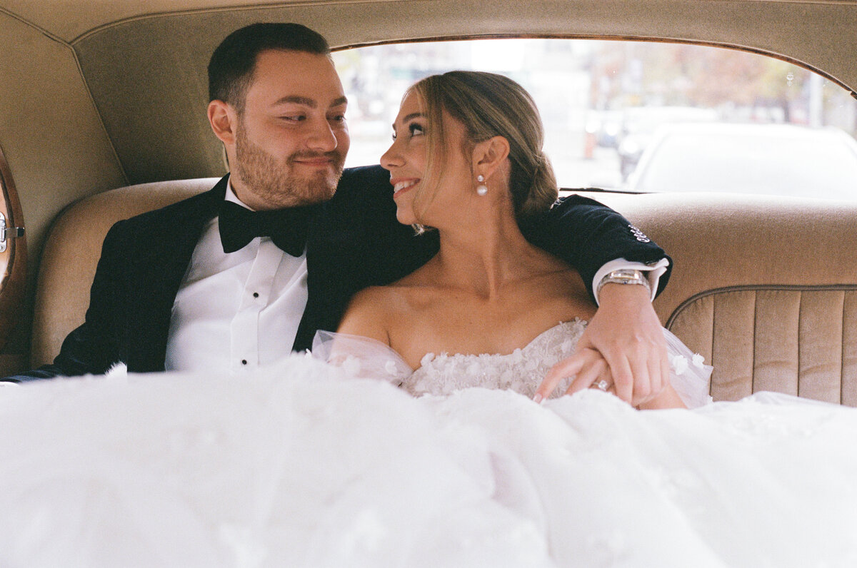 A grainy film photo shot on 35mm of a couple in the back of a classic car on their wedding day
